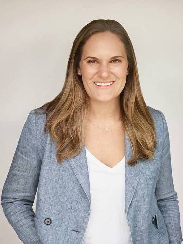 A woman with long hair wearing a gray blazer and white shirt.