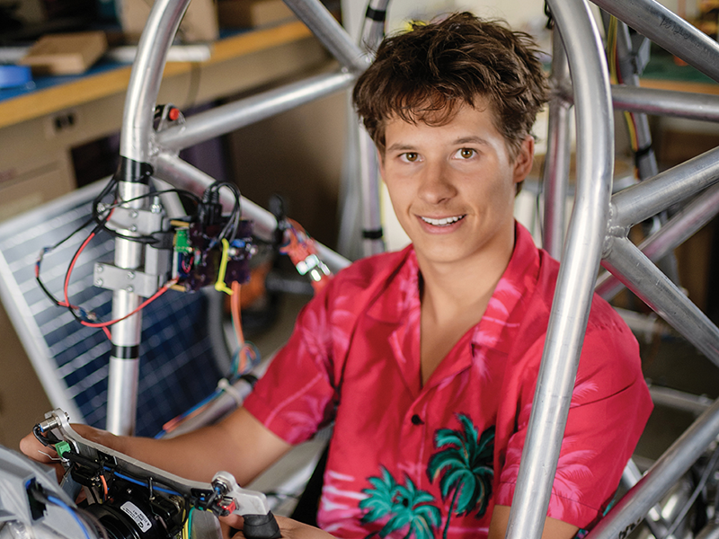 A person with short brown hair wearing a pink Hawaiian shirt sitting in a DIY car
