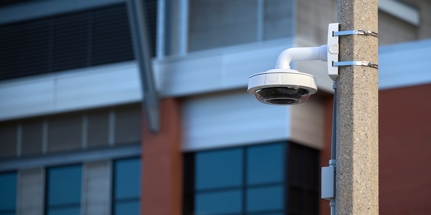 A picture of a white circular video camera attached with metal clamps to a stone pole