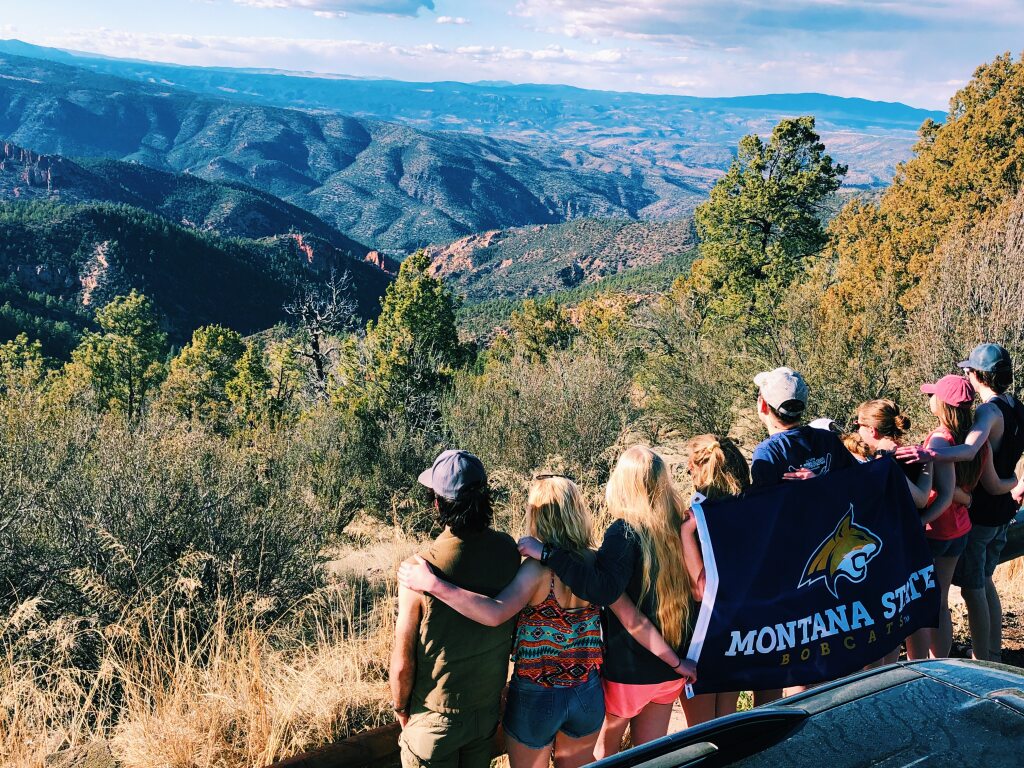 Group of Students Holding a Flag facing away from camera looking at valley below.