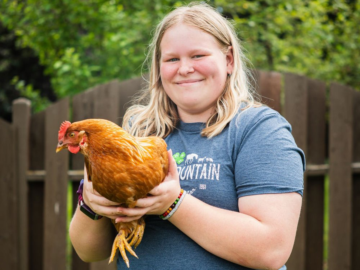 A 4-H member with long blonde hair holding an orange chicken