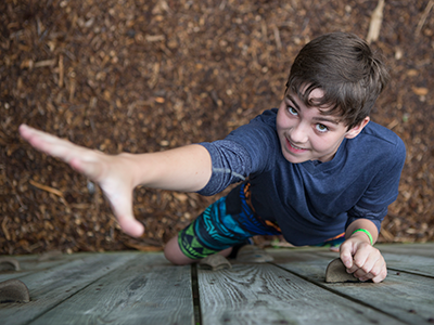 A boy climbing on a wall reaching toward the camera