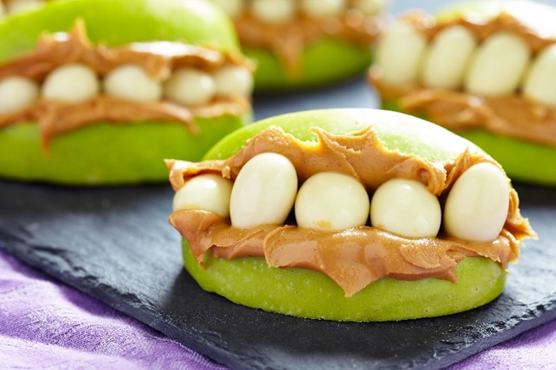 Four apple smiles made with green apples, peanut butter, and yogurt covered raisins. 