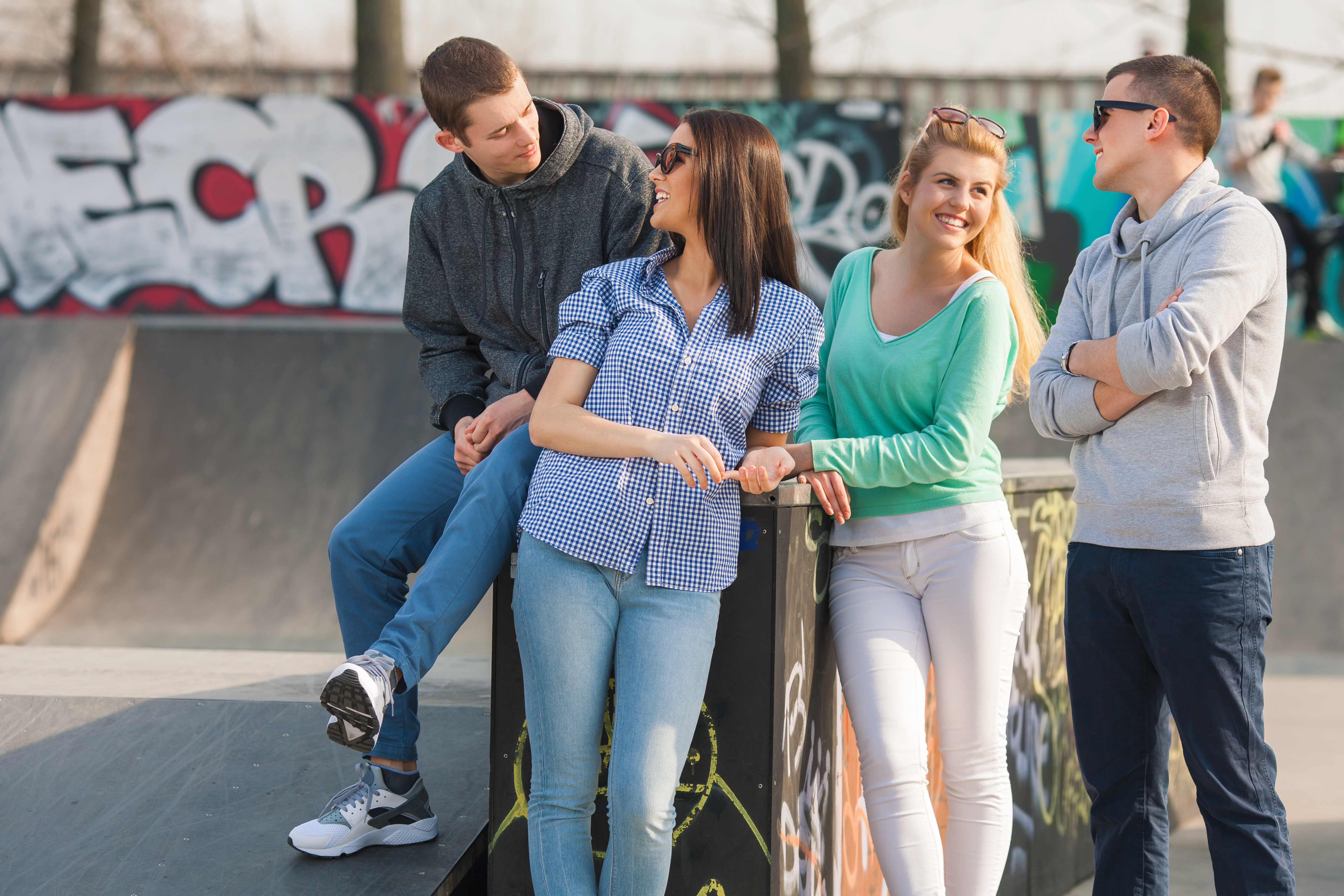 A group of teens standing and smiling at each other at a skate park
