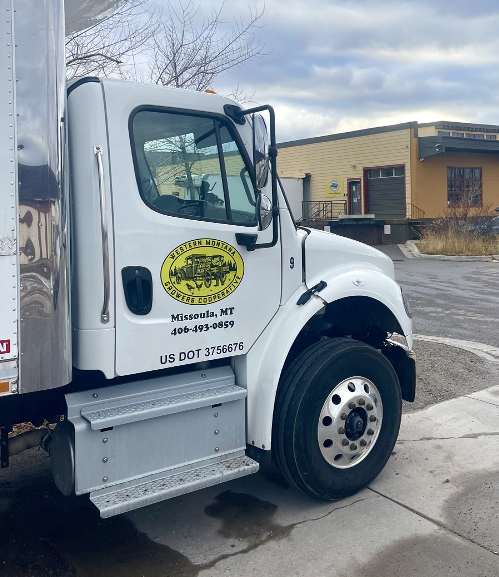 A white cab of a semi truck is parked and displays a yellow Western Montana Growers Cooperative logo on the door.