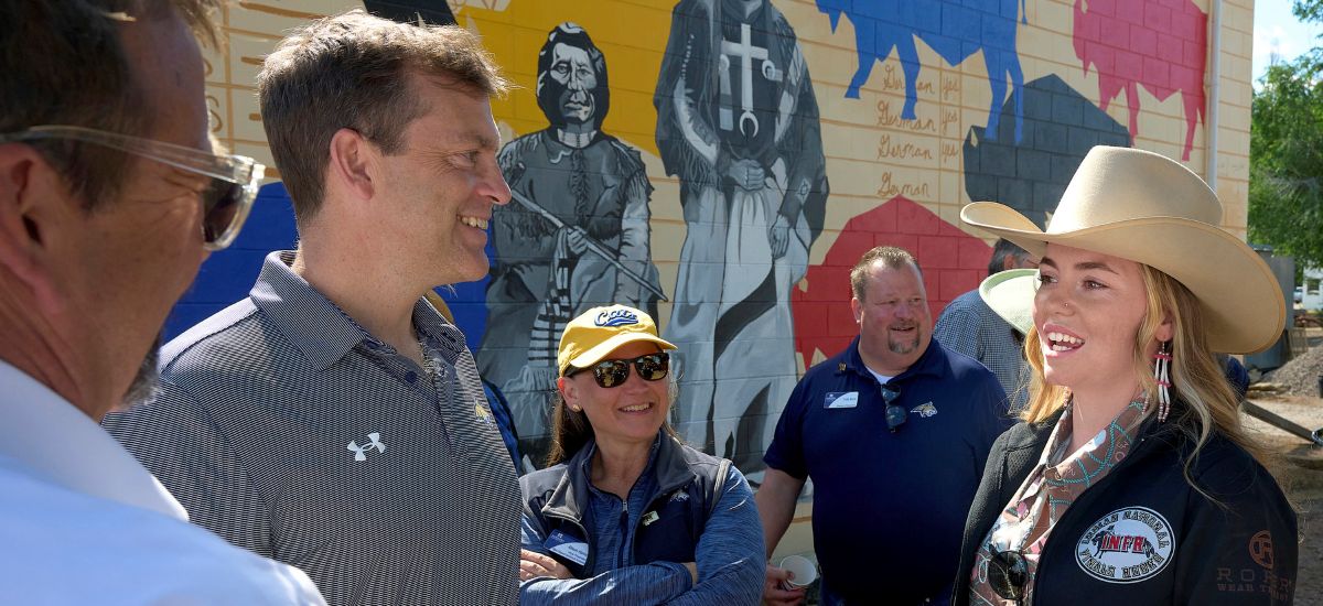 Several people standing and talking outdoors in front of a colorful mural painted on a building wall.