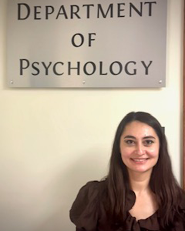 A person with glasses and a scarf on with trees in the background