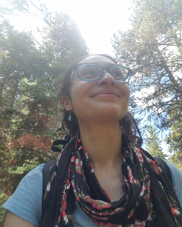 A person with glasses and a scarf on with trees in the background