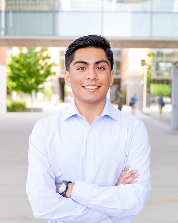 A man with black hair and a light blue long sleeved button up with his arms folded