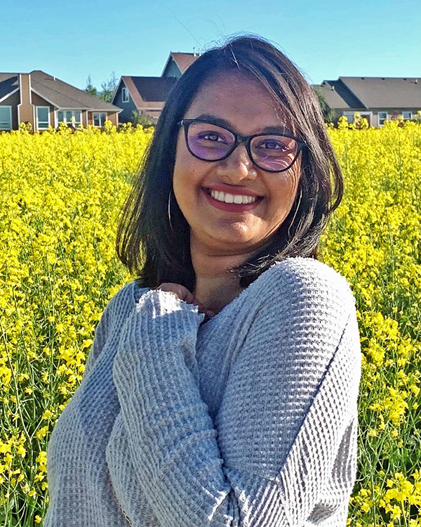 A person with long brown hair wearing a gray long sleeved shirt and glasses