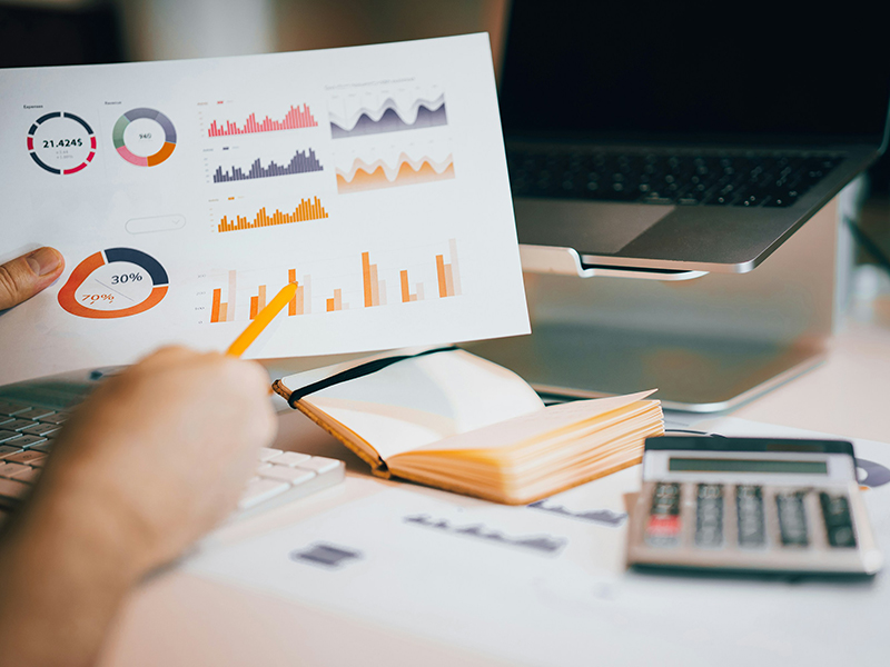 A stock image of a person holding a pencil and papers with pie charts and bar graphs on them