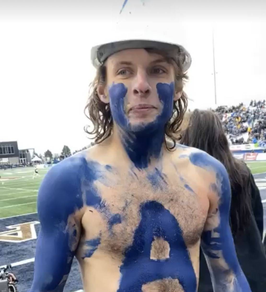 Male student at a football game. His chest and arms are painted blue in support of the Bobcats