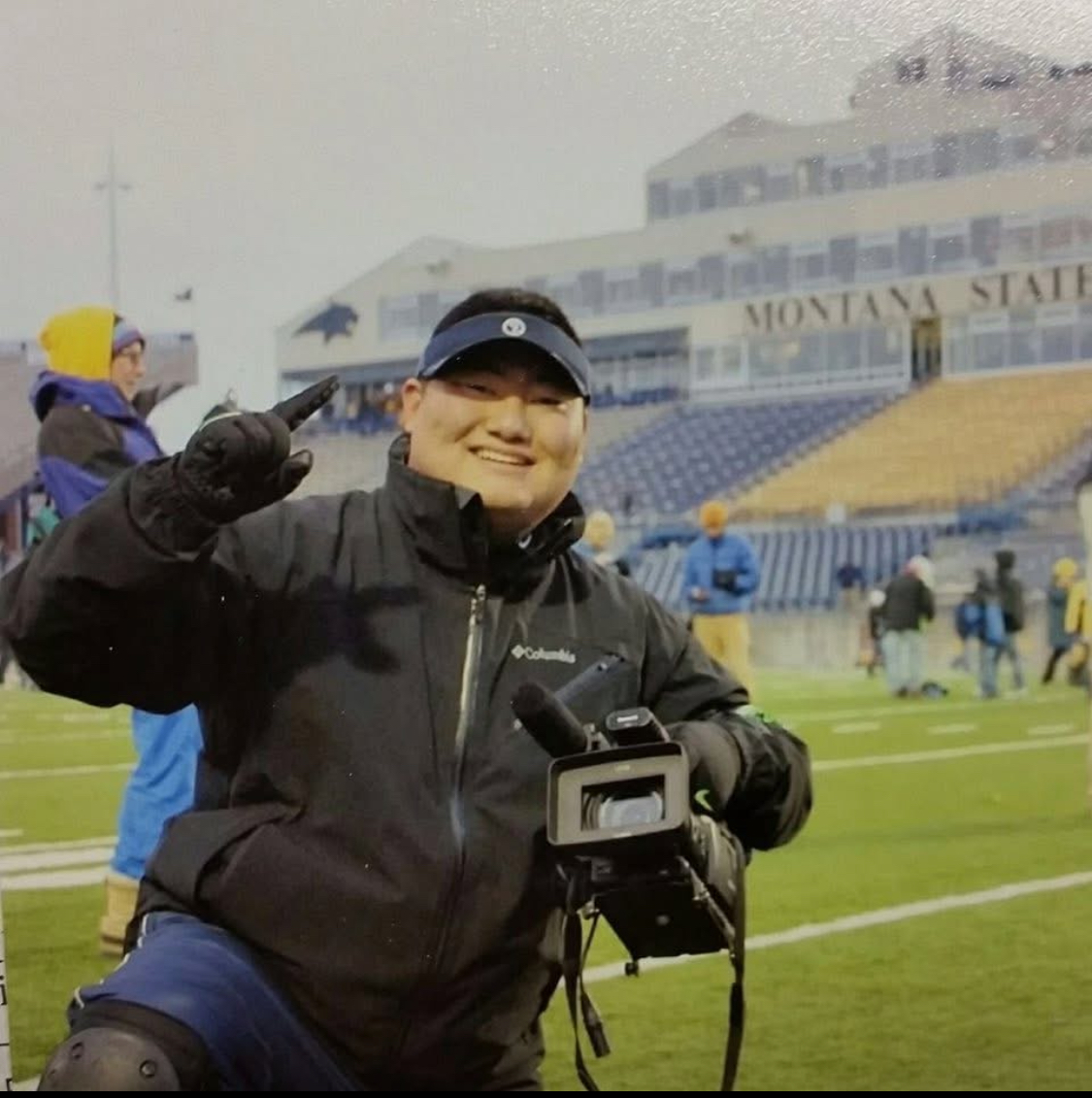 Male student holding a video camera on the football field.