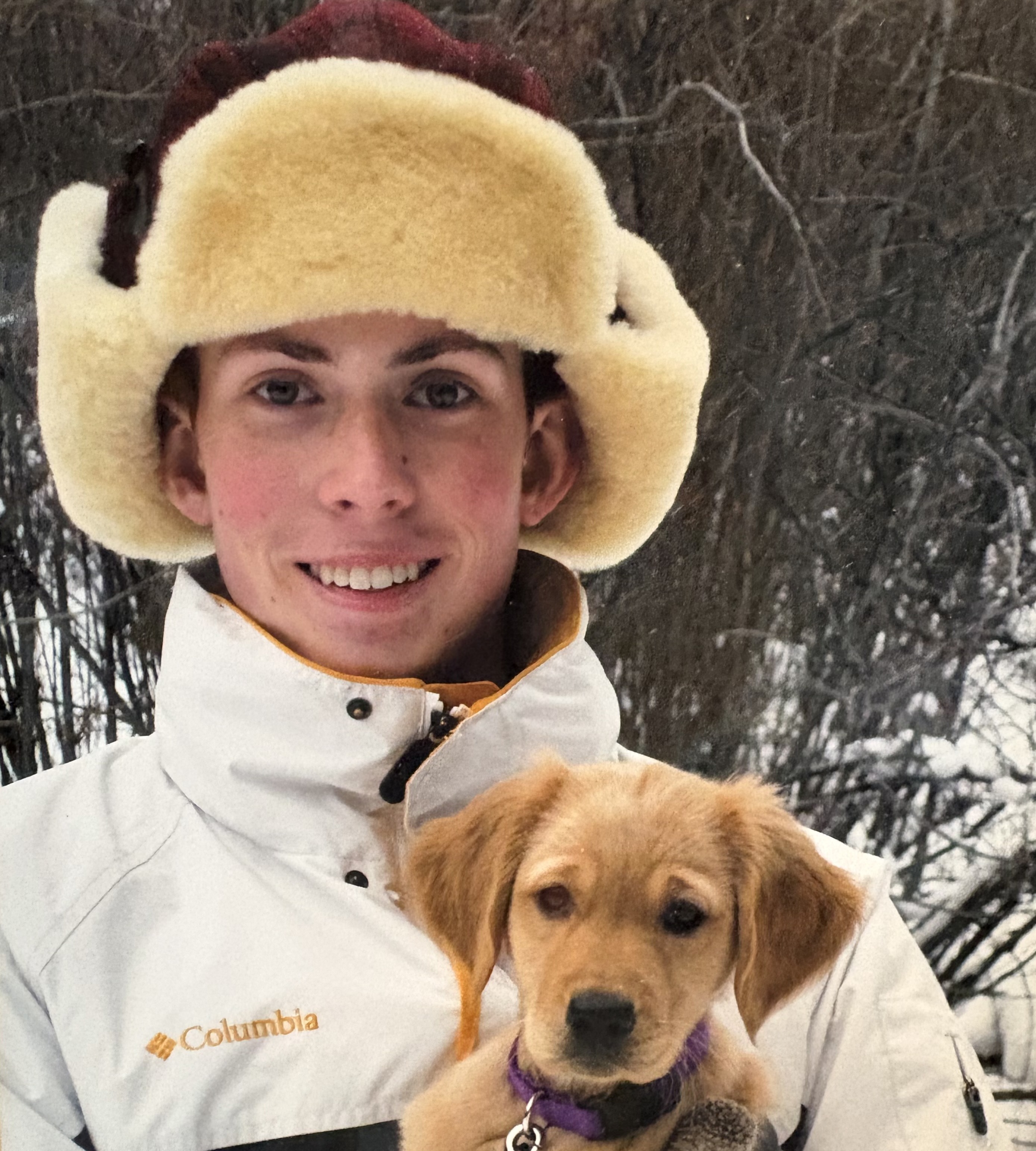 Male student wearing a inter hat and coat while holding a puppy