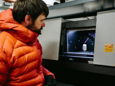 photo of Kevin Hammonds in orange coat standing next to microCT machine