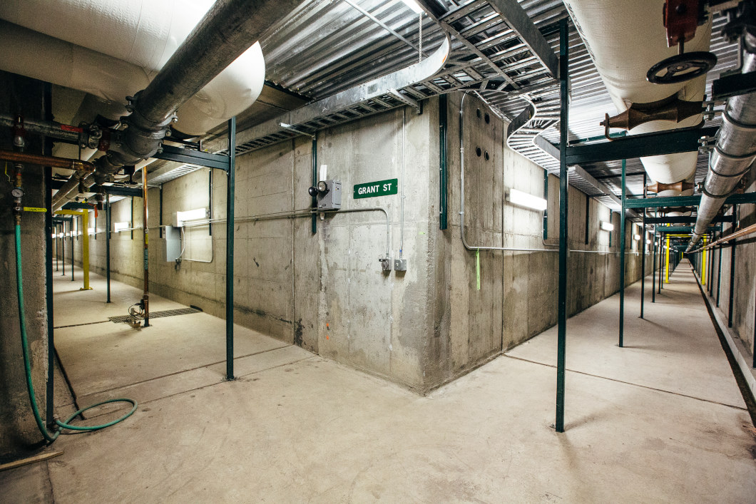 Two hallways connecting at a corner. Concrete walls and floors with pipes up and down.