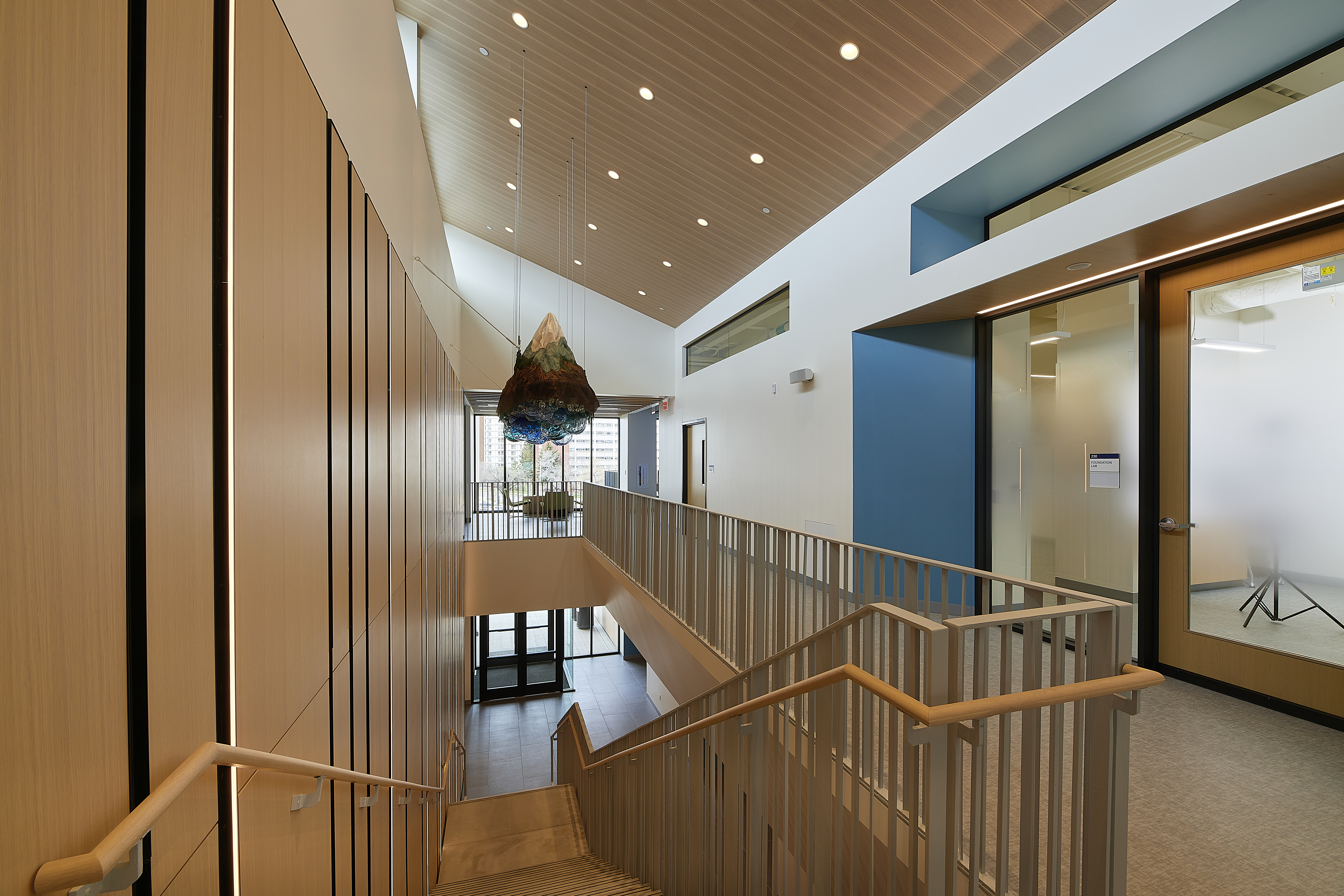 A picture taken from the second story of a building looking down a wooden stairwell. There are classrooms on one side of the second story wall.