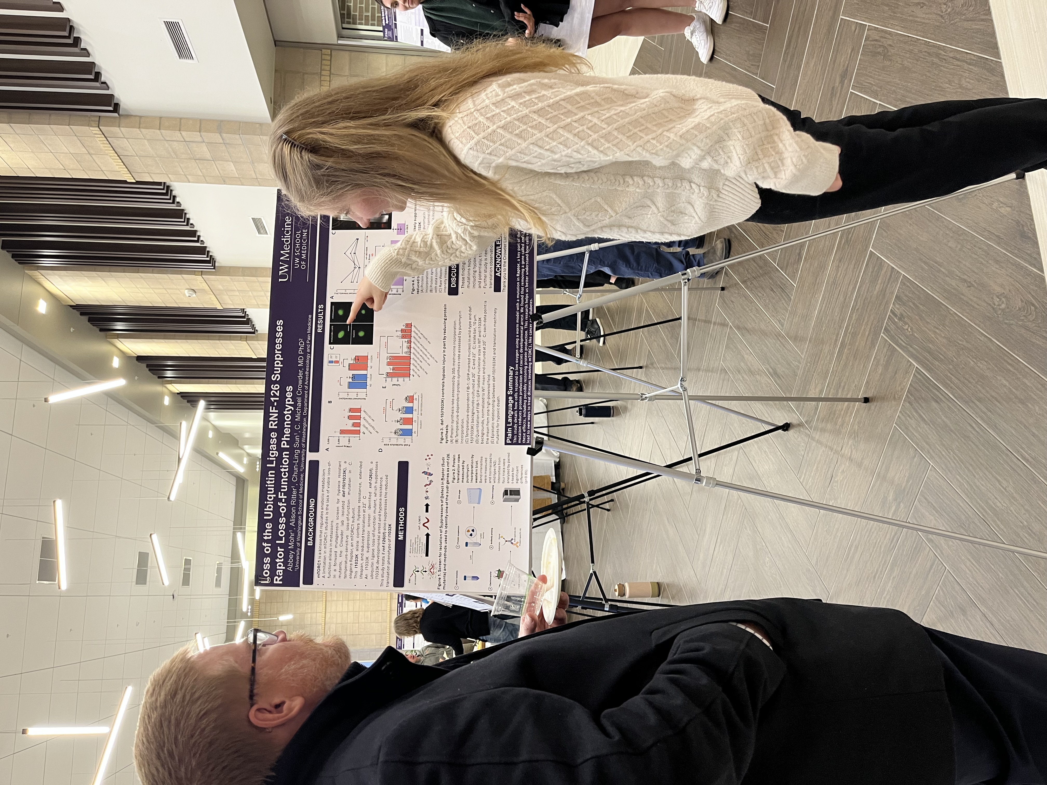 Photo of a female medical student pointing to a chart on a research poster while a man looks on